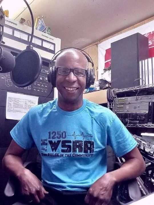TCB smiling in a blue WSRA shirt beside the studio microphone