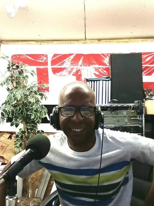 TCB smiling in a striped shirt at the microphone